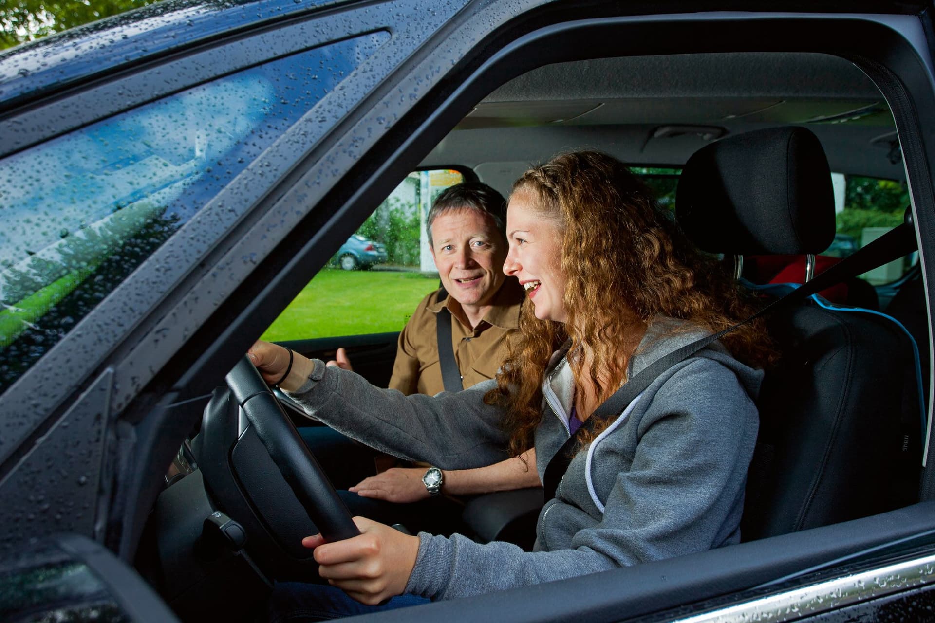 Frau und Mann sitzen im Auto, beide lachen.