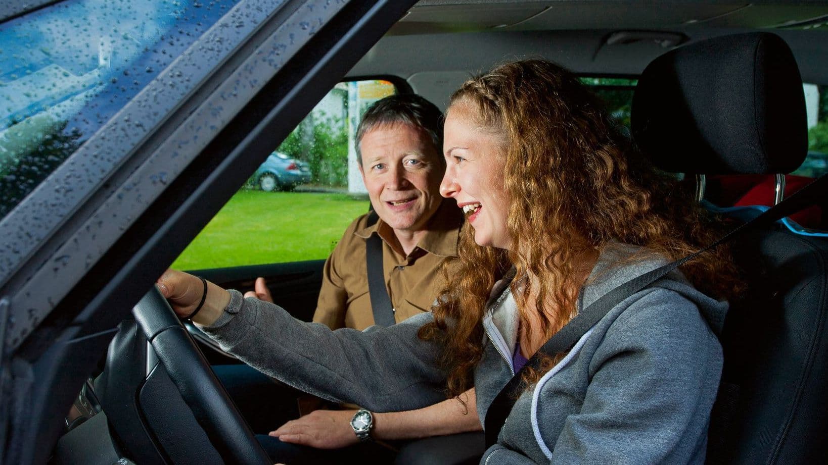 Frau und Mann sitzen im Auto, beide lachen.