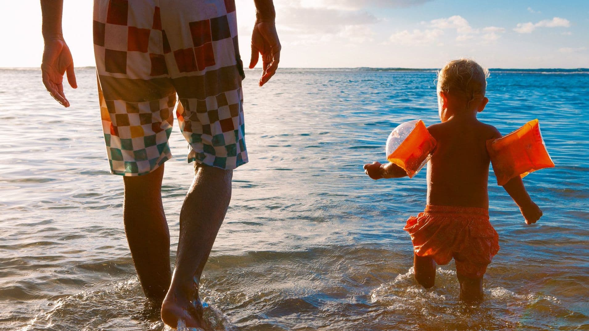 Mann und Kleinkind gehen ins Meer.