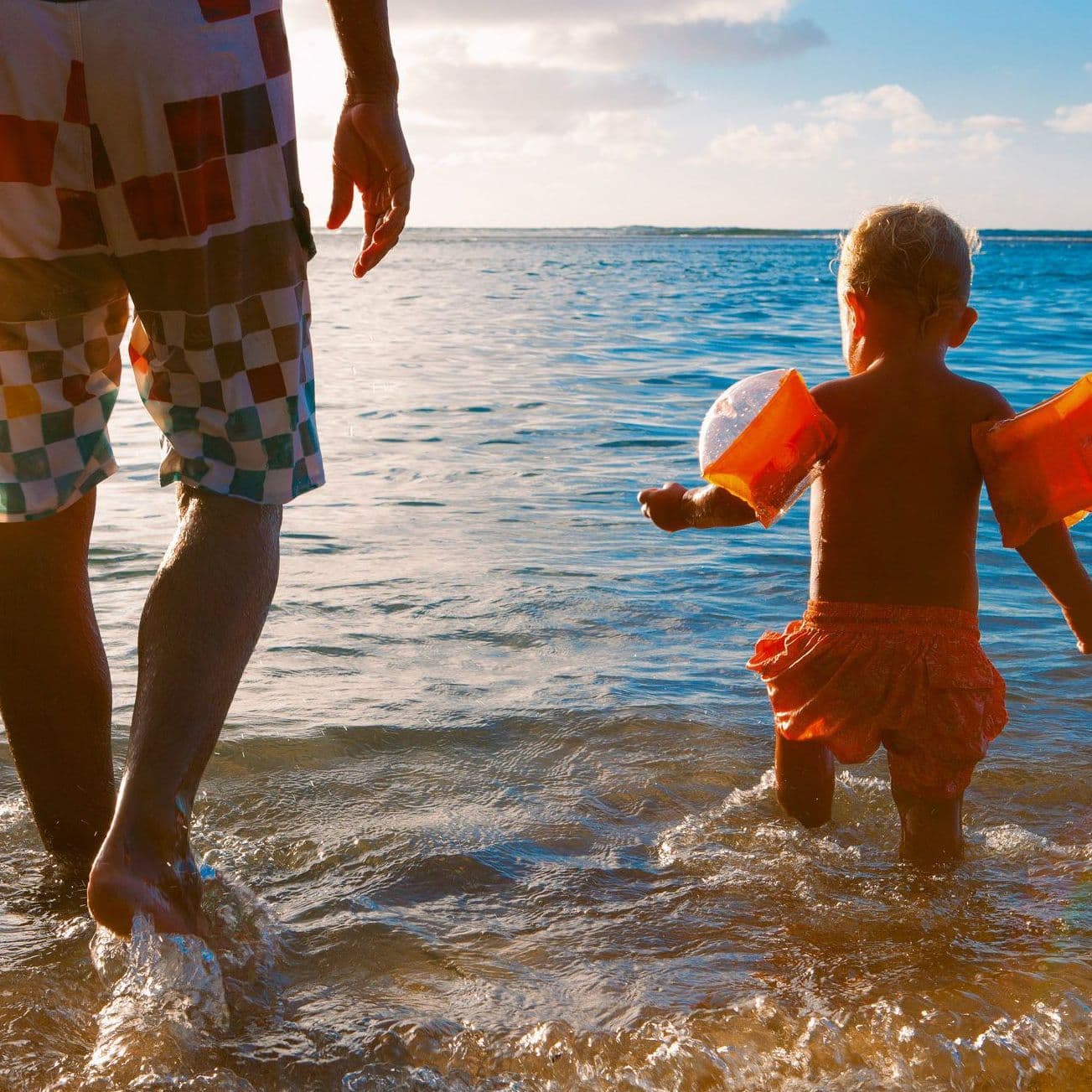 Mann und Kleinkind gehen ins Meer.