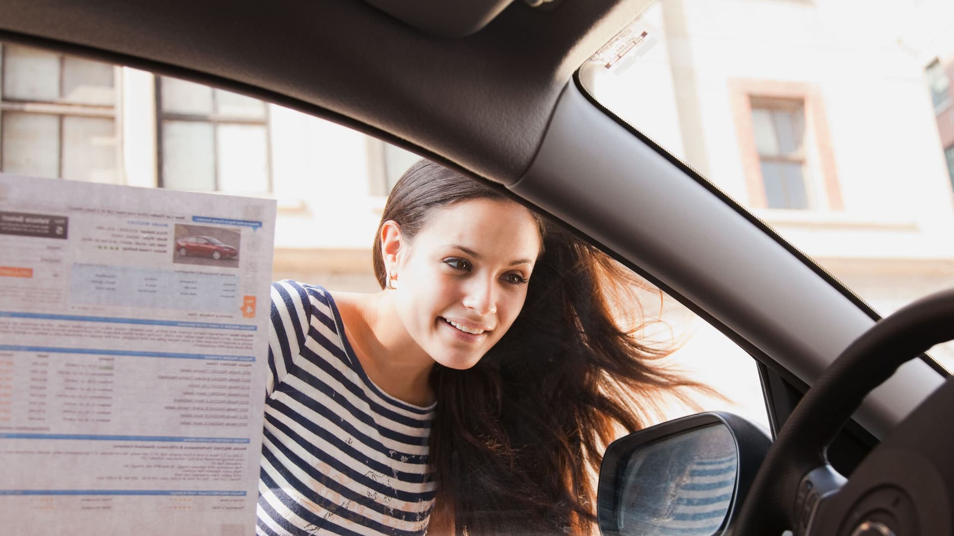 Junge Frau blickt in ein Auto und lächelt.