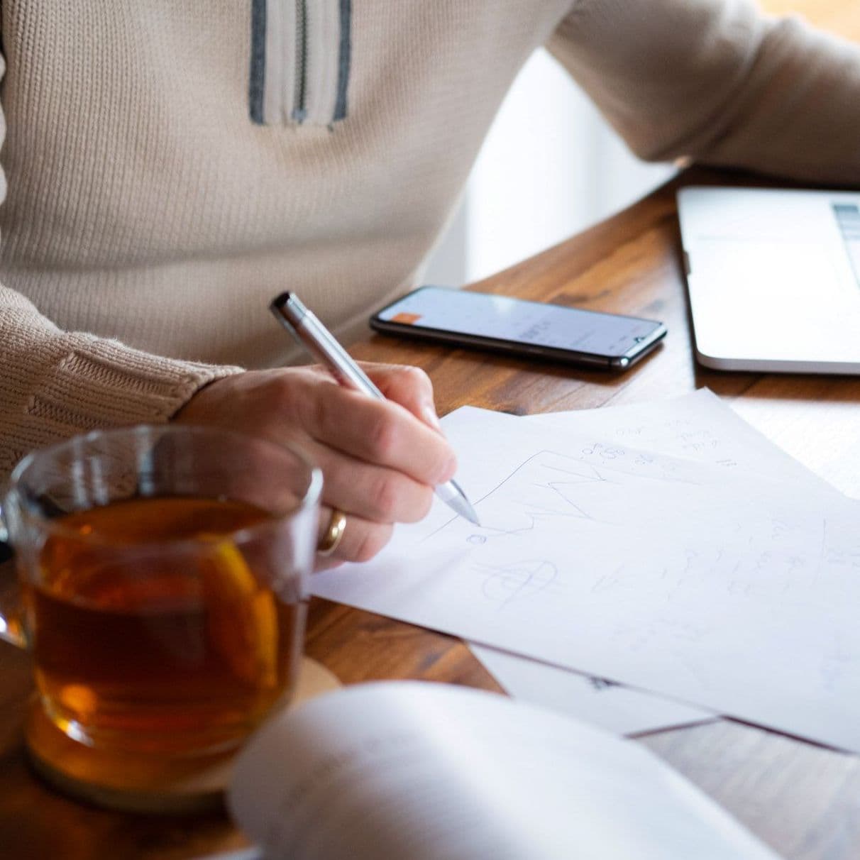 Jemand sitzt am Tisch mit Laptop, Handy und Notizen.