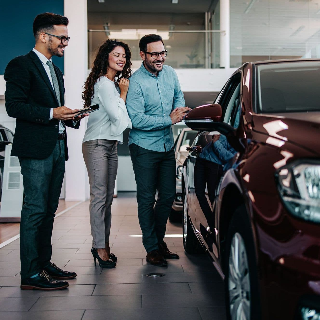 Verkäufer und zwei Interessenten stehen im Autohaus und betrachten ein Auto.