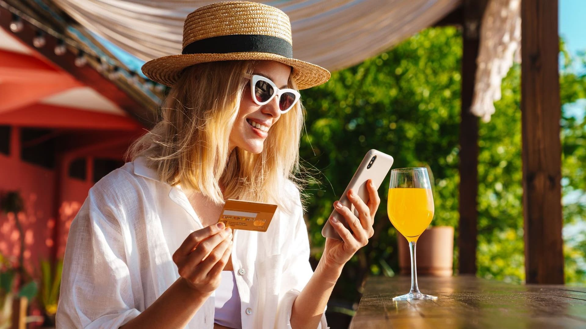 Frau blickt lächelnd auf ihr Handy, die Bezahlkarte in der Hand.