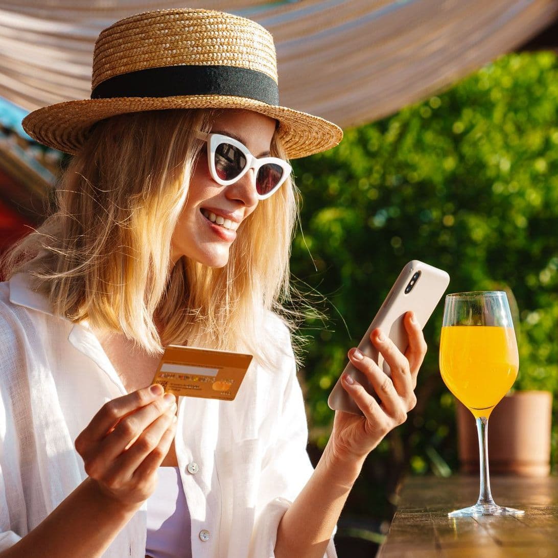 Frau blickt lächelnd auf ihr Handy, die Bezahlkarte in der Hand.