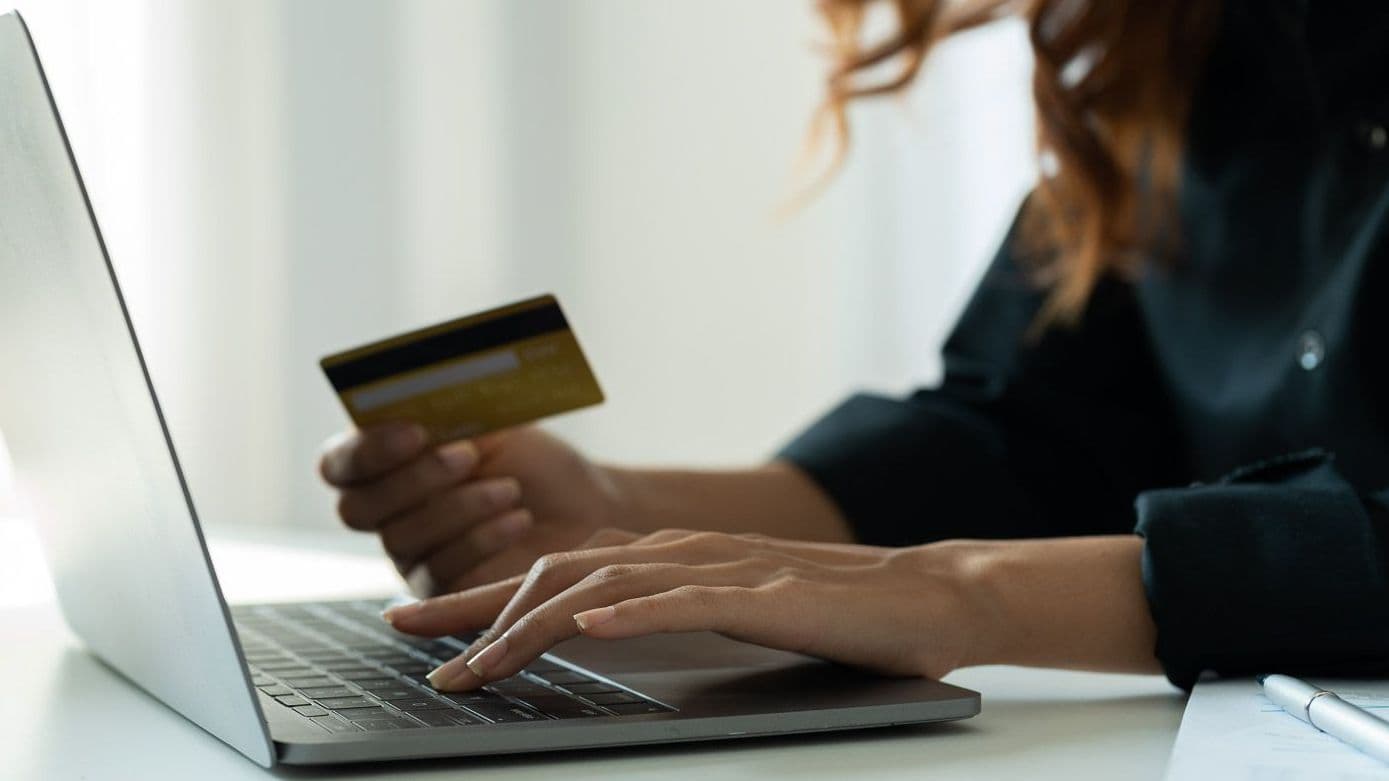 Frau tippt am Laptop, die Bezahlkarte in der Hand.