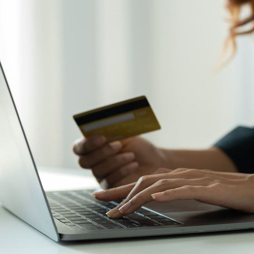 Frau tippt am Laptop, die Bezahlkarte in der Hand.