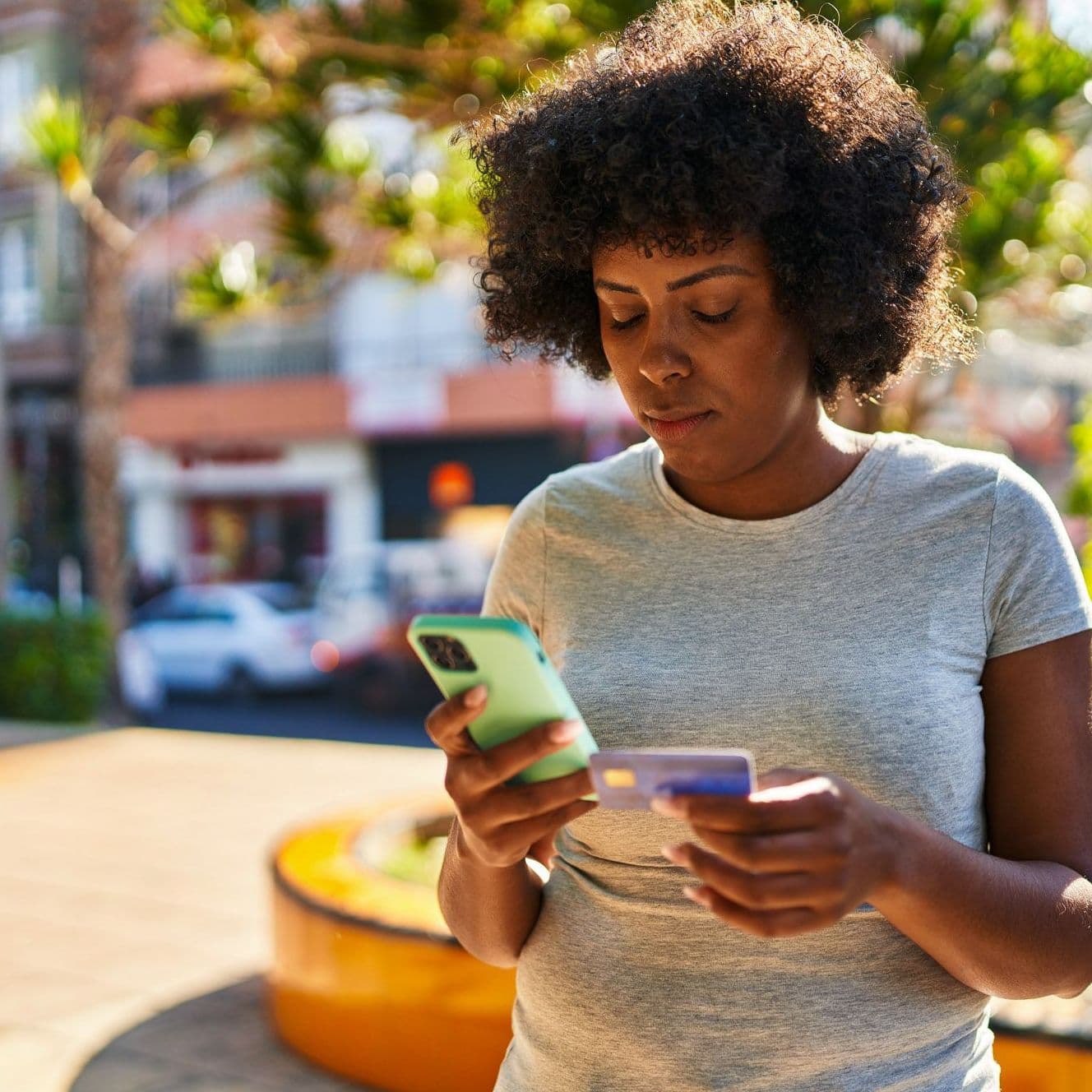Junge Frau blickt auf ihr Handy und hat eine Bezahlkarte in der Hand.