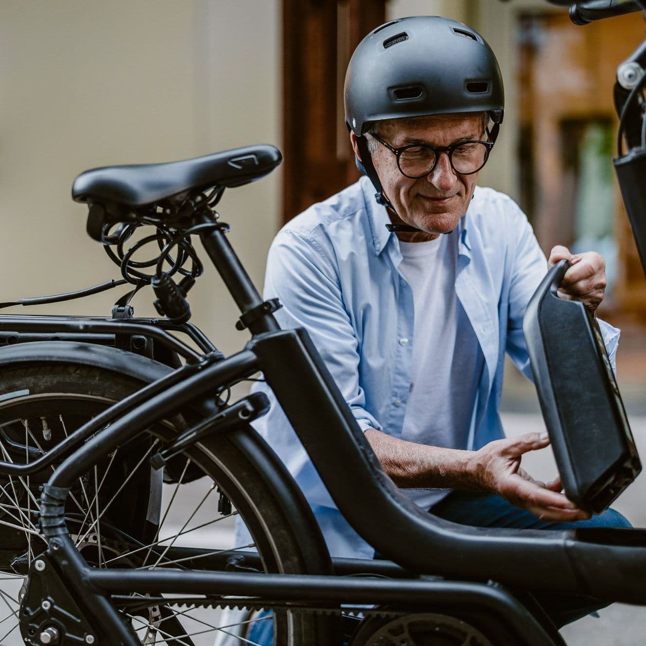 Mann mit Helm hockt neben E-Bike und hält einen Akku in der Hand