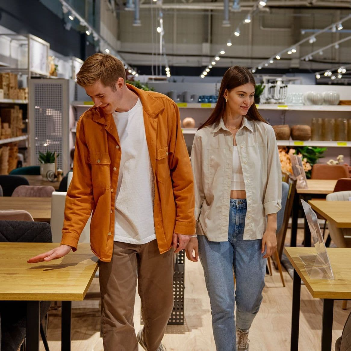 Zwei Junge Leute laufen im Möbelhaus durch die Tischabteilung.