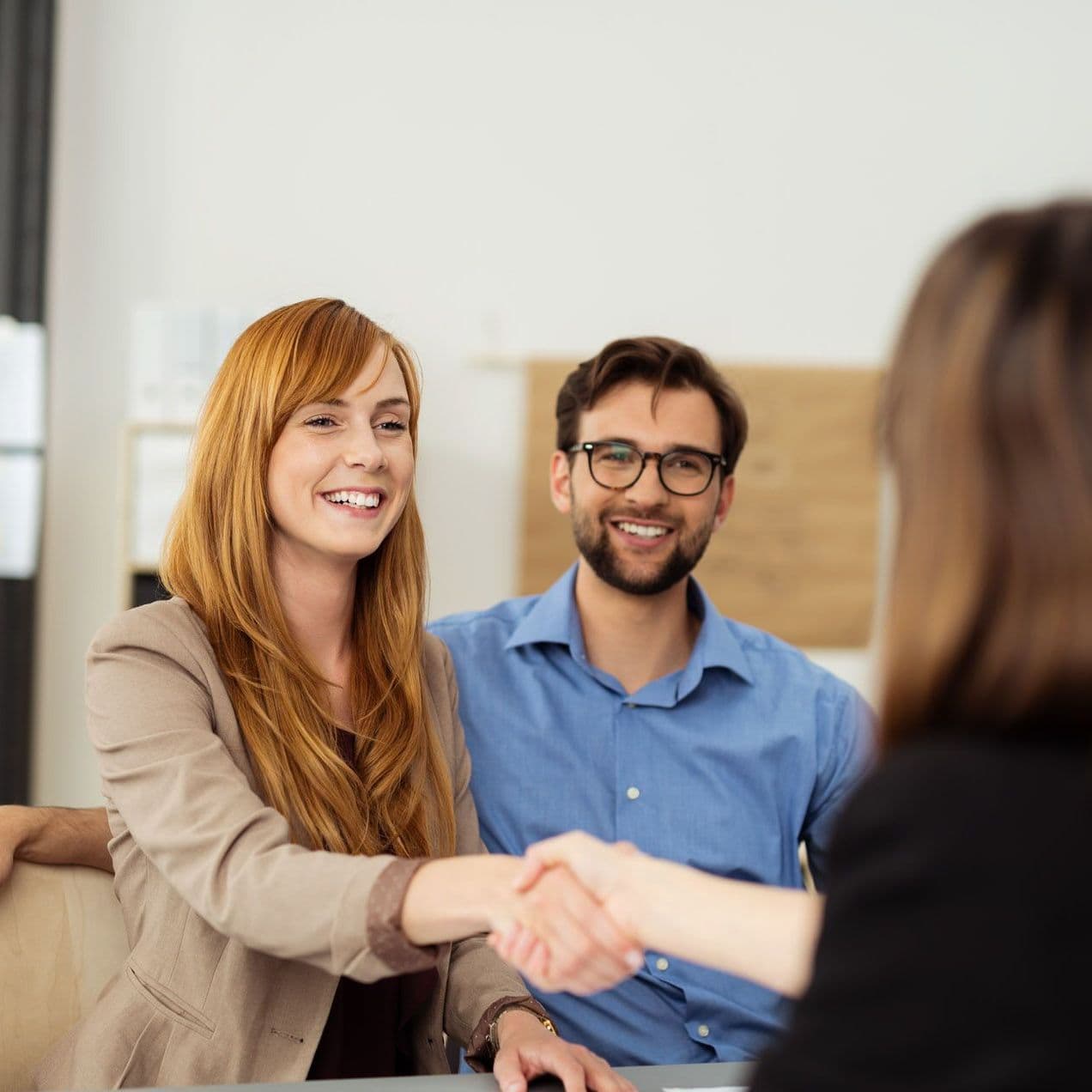 Zwei Frauen schütteln Hände, ein Mann sitzt daneben.
