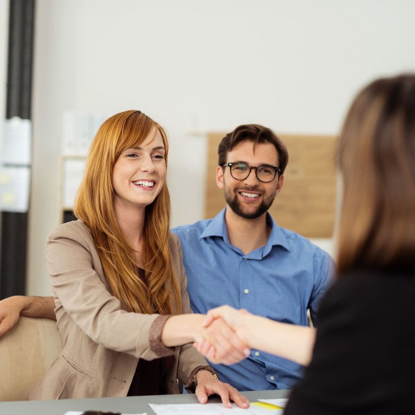 Zwei Frauen schütteln Hände, ein Mann sitzt daneben.
