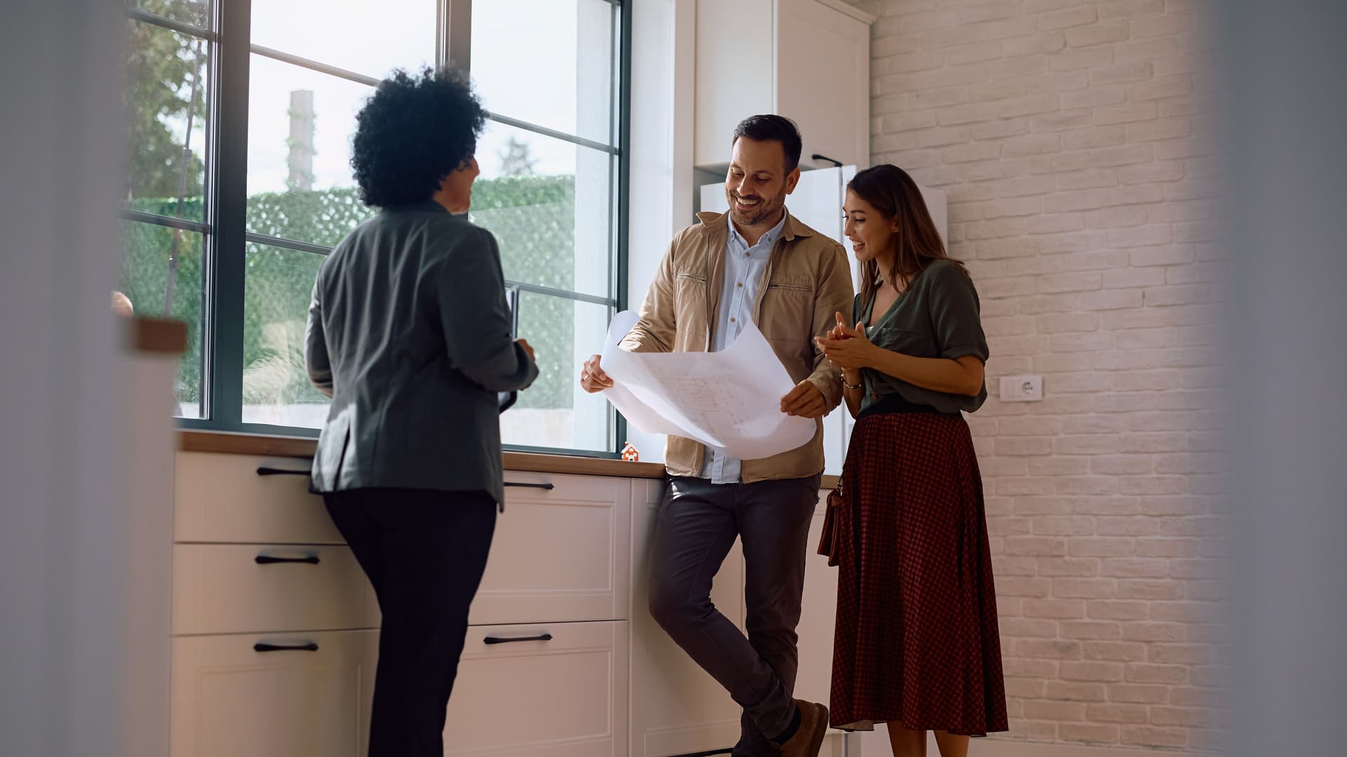 Maklerin und zwei weitere Personen stehen in einem Raum.