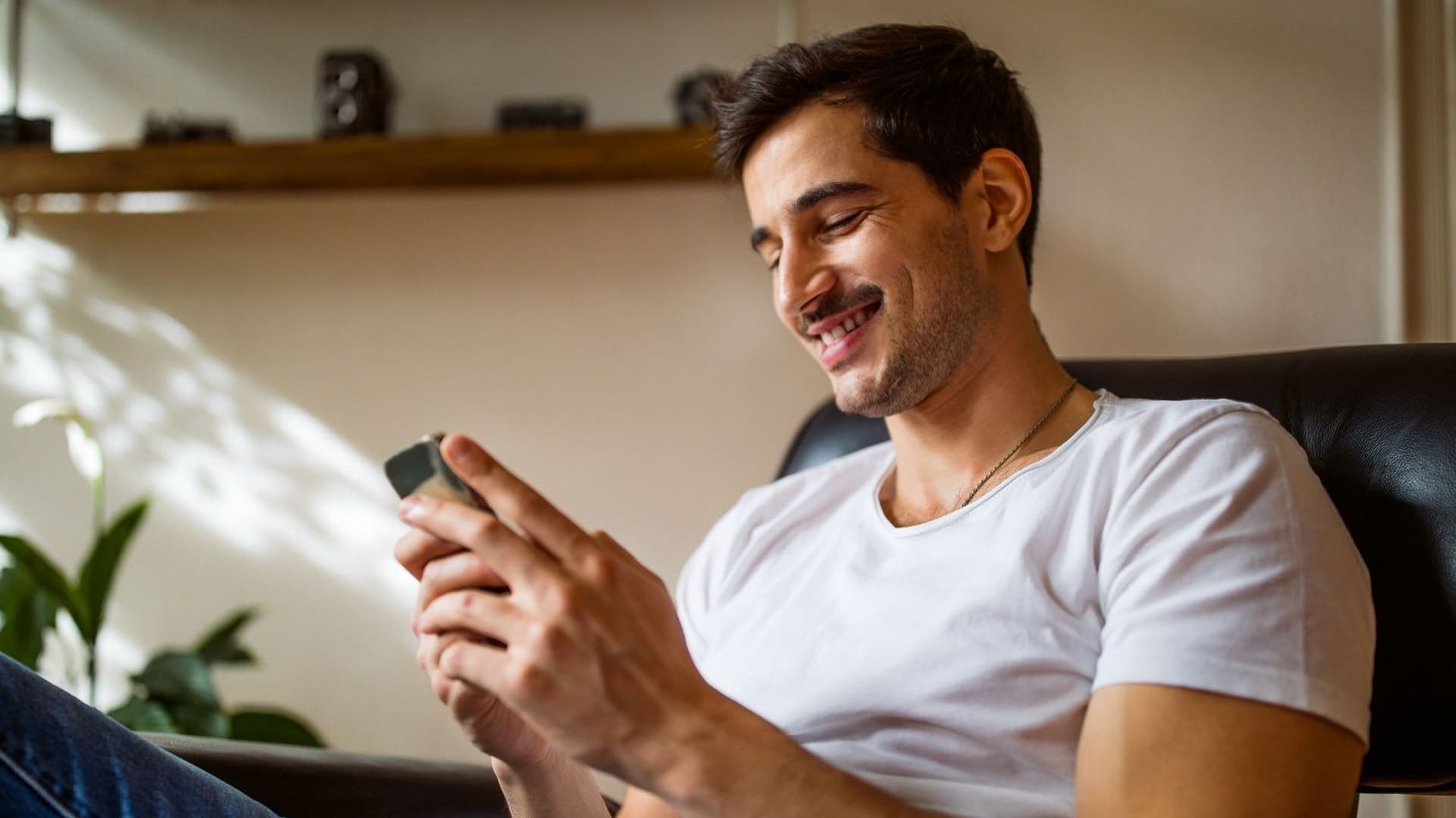 Junger Mann blickt auf sein Handy und lächelt.