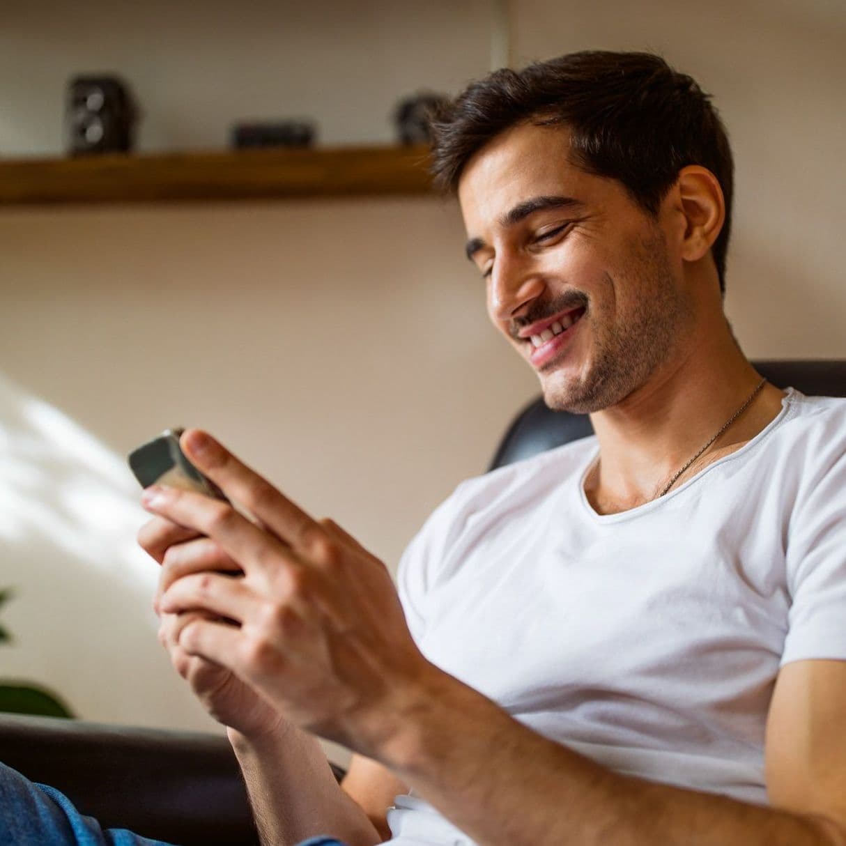 Junger Mann blickt auf sein Handy und lächelt.