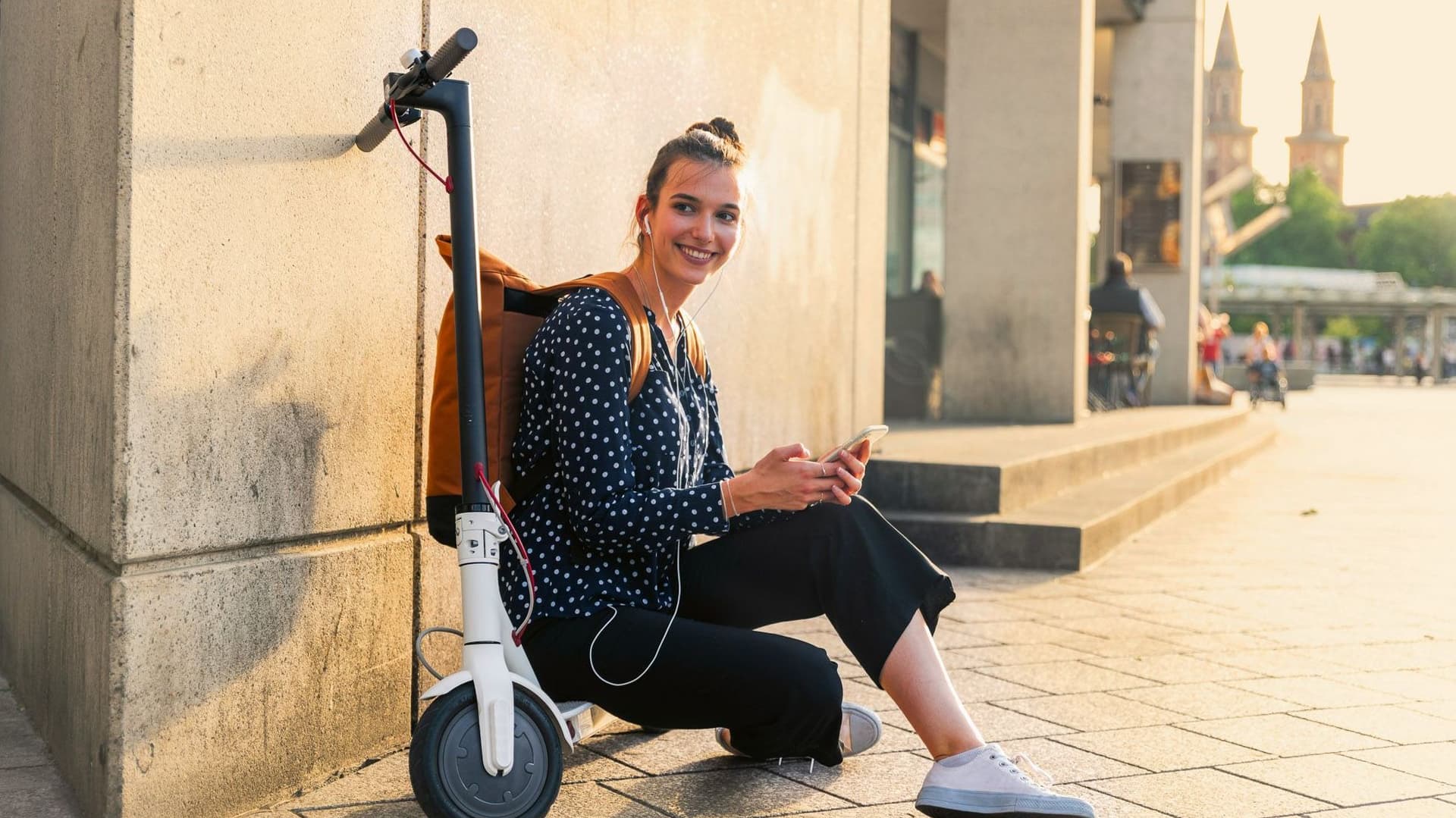Junge Frau sitzt auf einem Roller neben einem Gebäude.