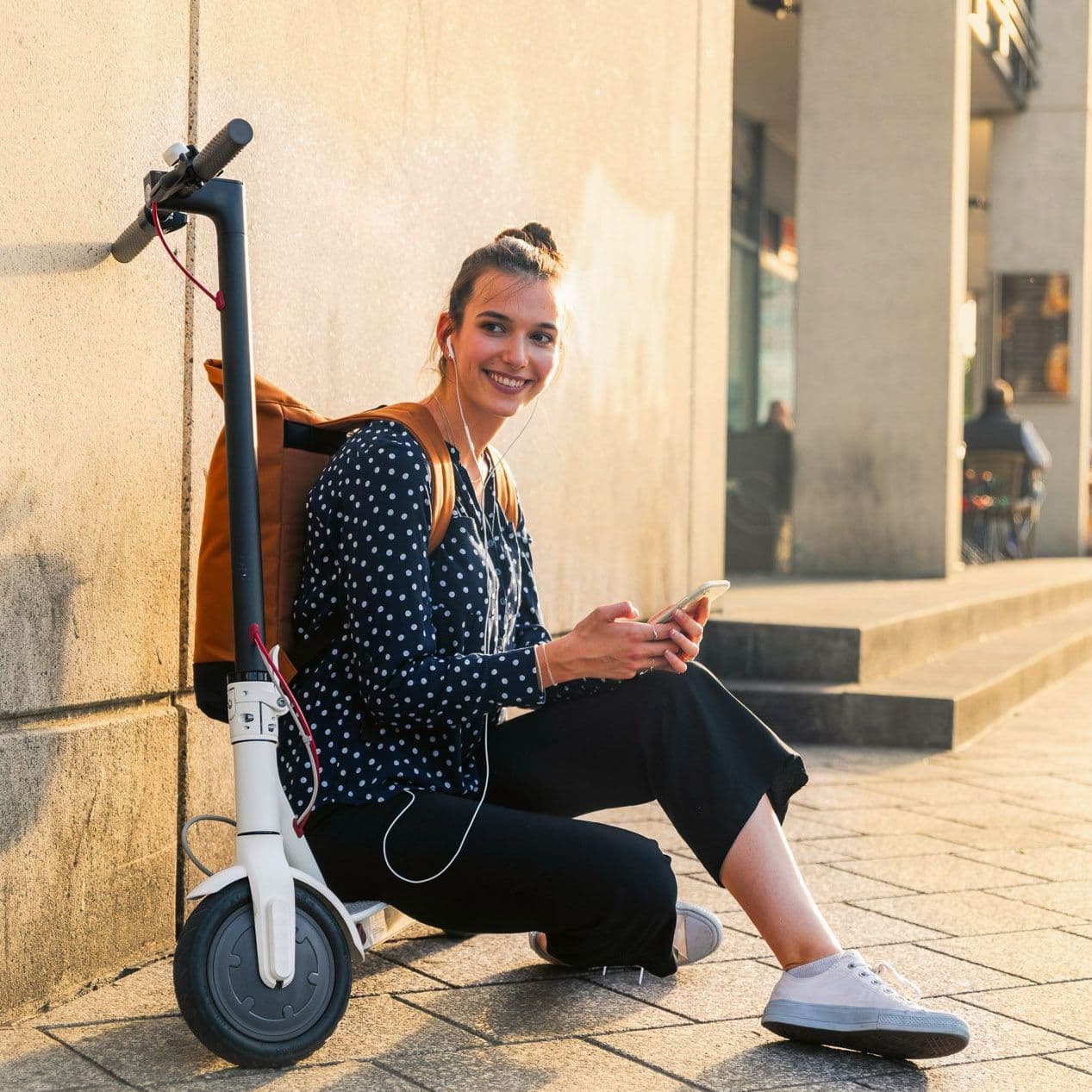Junge Frau sitzt auf einem Roller neben einem Gebäude.