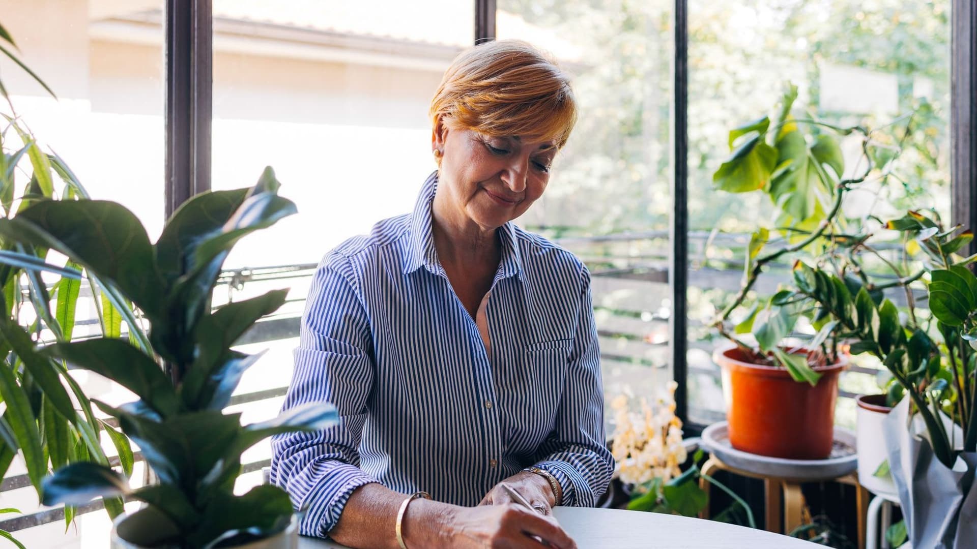 Frau sitzt am Tisch und schreibt auf ein Blatt Papier.