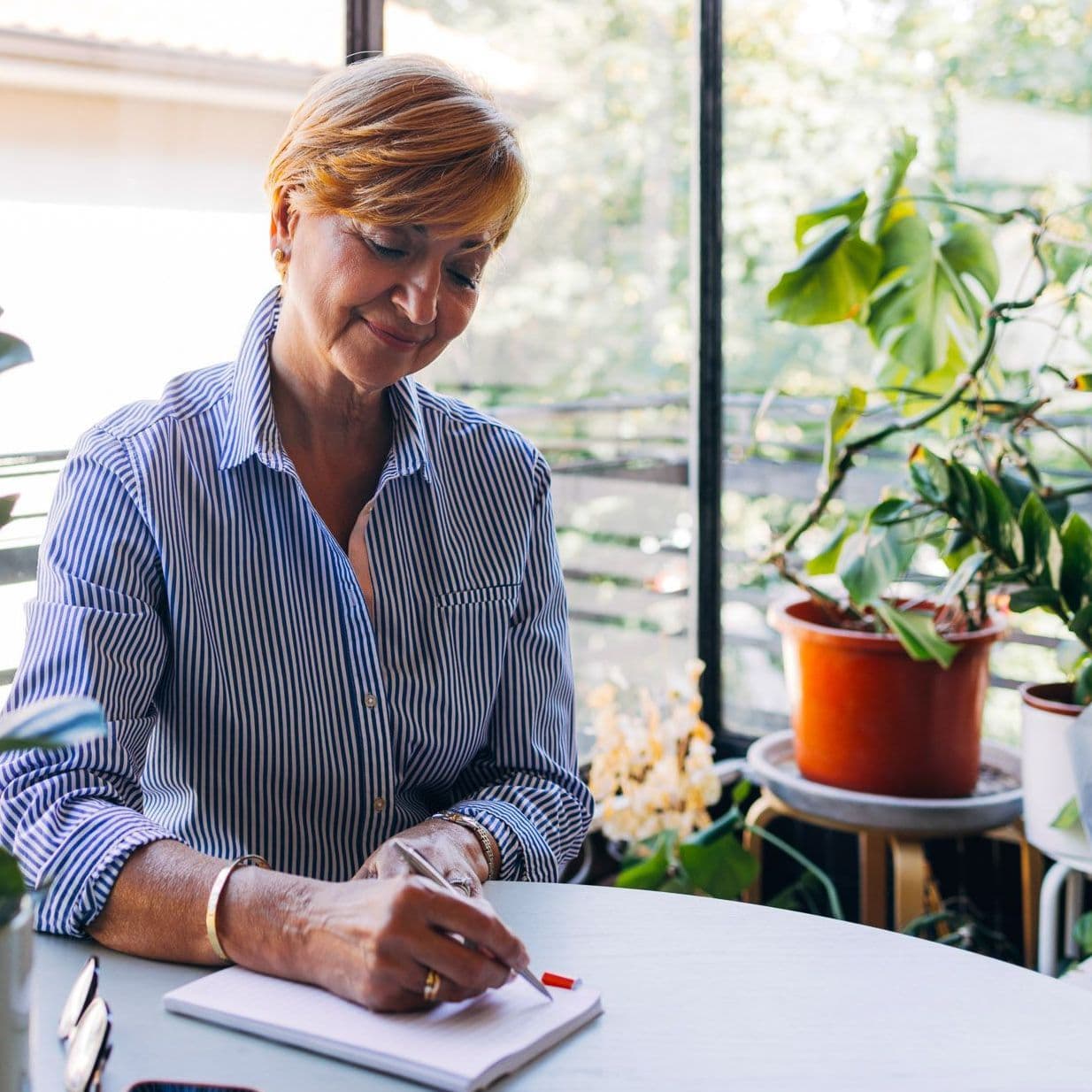 Frau sitzt am Tisch und schreibt auf ein Blatt Papier.