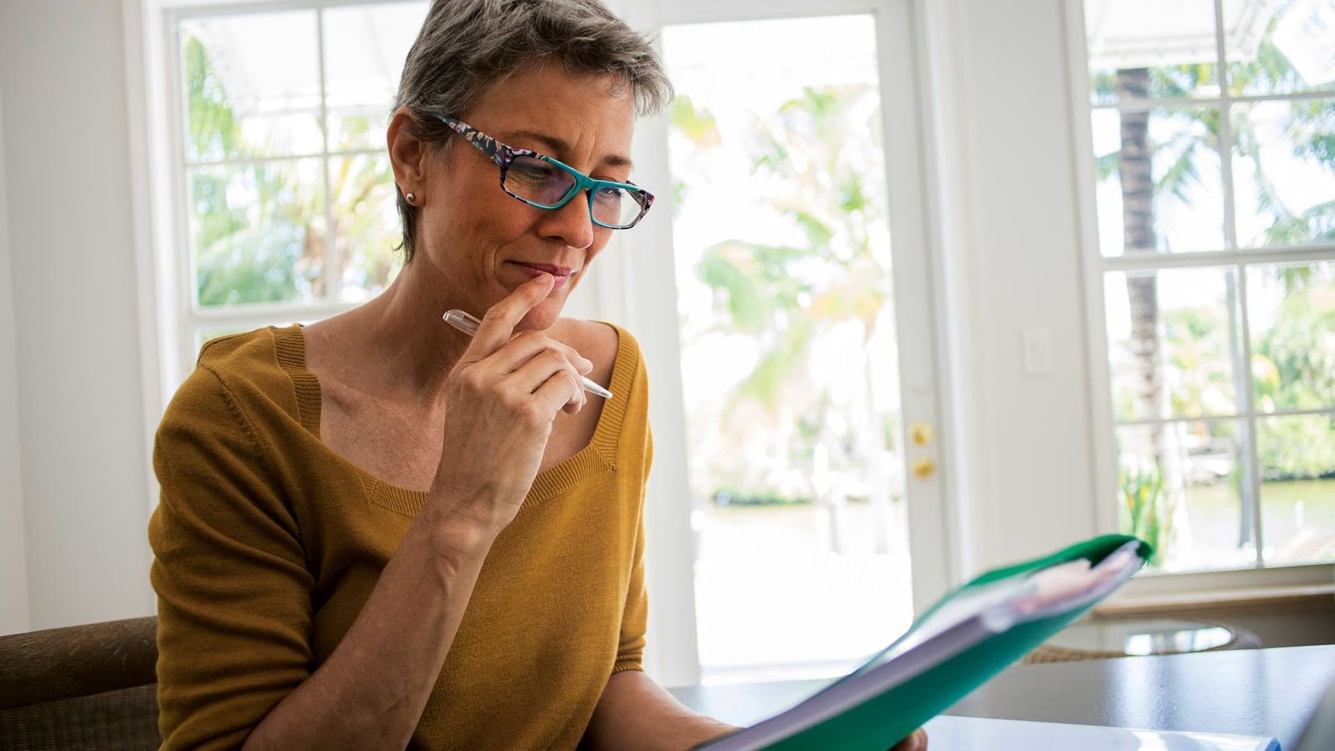 Frau sitzt am Laptop und betrachtet eine Mappe.