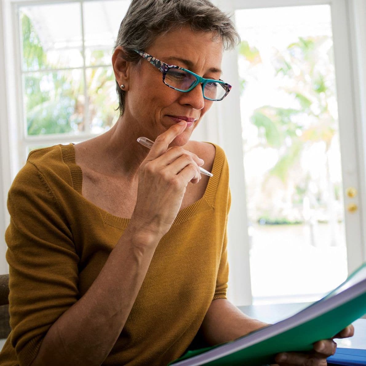 Frau sitzt am Laptop und betrachtet eine Mappe.
