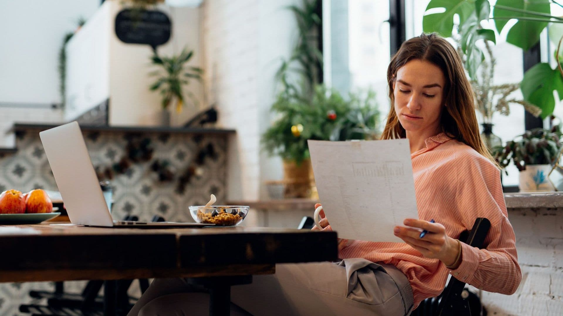 Frau sitzt am Tisch und betrachtet ein Blatt Papier.