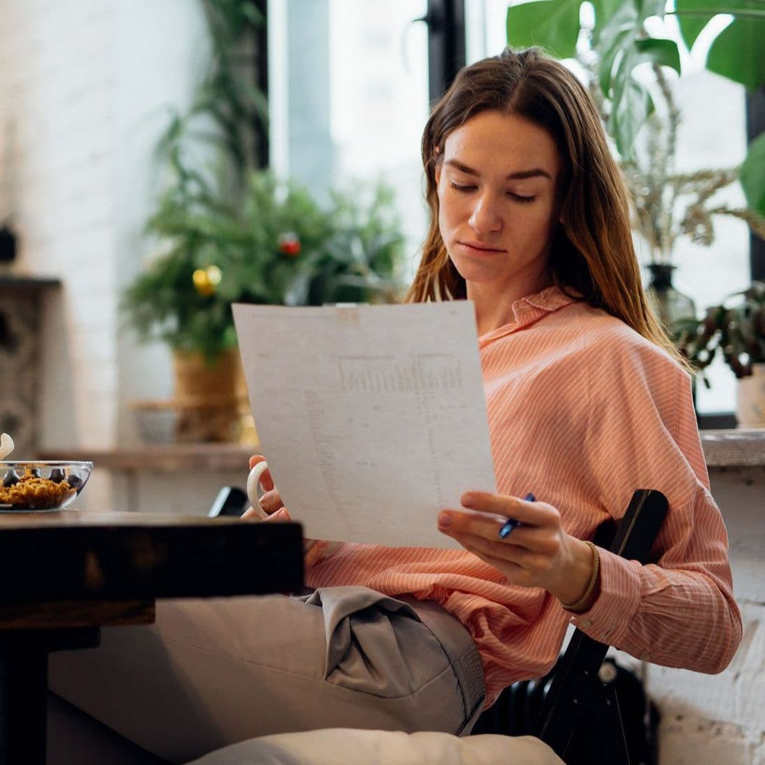 Frau sitzt am Tisch und betrachtet ein Blatt Papier.