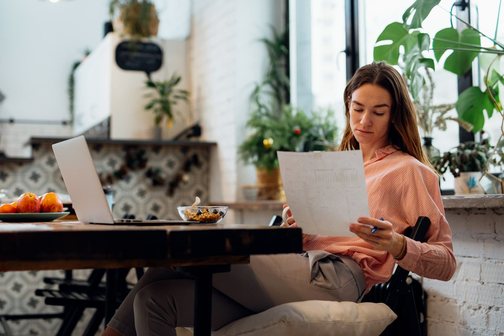 Frau sitzt am Tisch und betrachtet ein Blatt Papier.