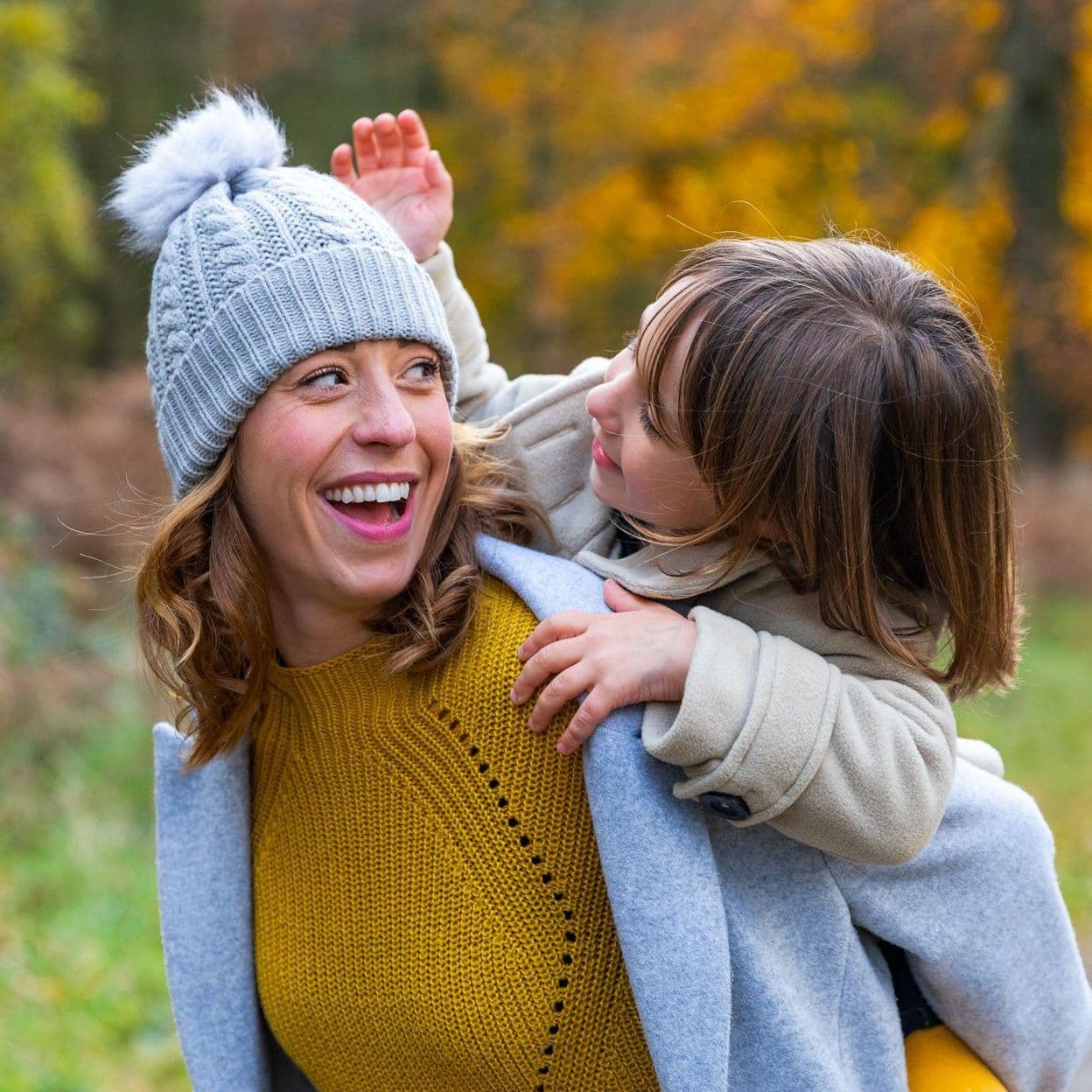 Junge Frau trägt Mädchen auf dem Rücken, herbstliche Umgebung.