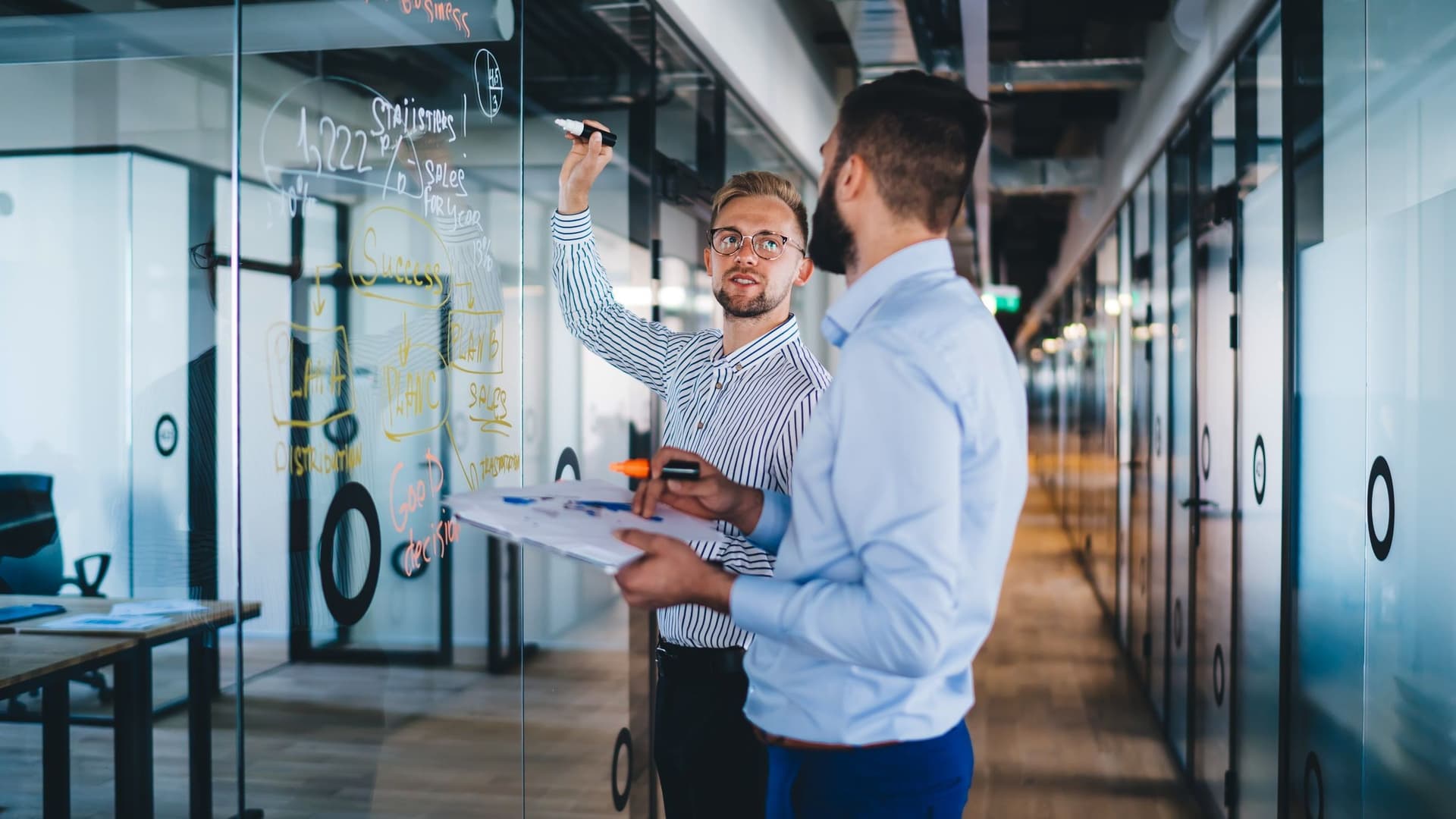 Zwei Männer im Büro schreiben an einer Glaswand.