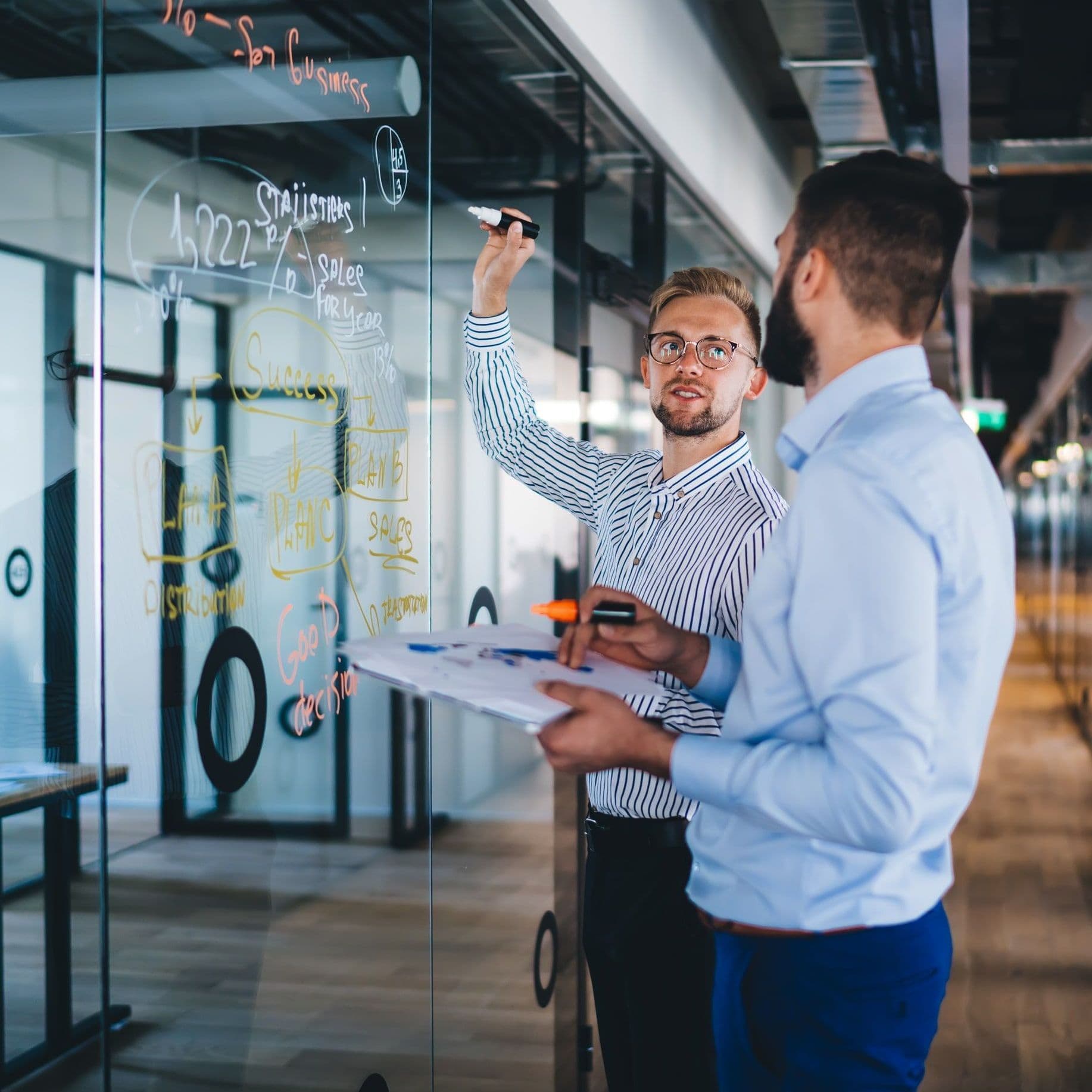 Zwei Männer im Büro schreiben an einer Glaswand.