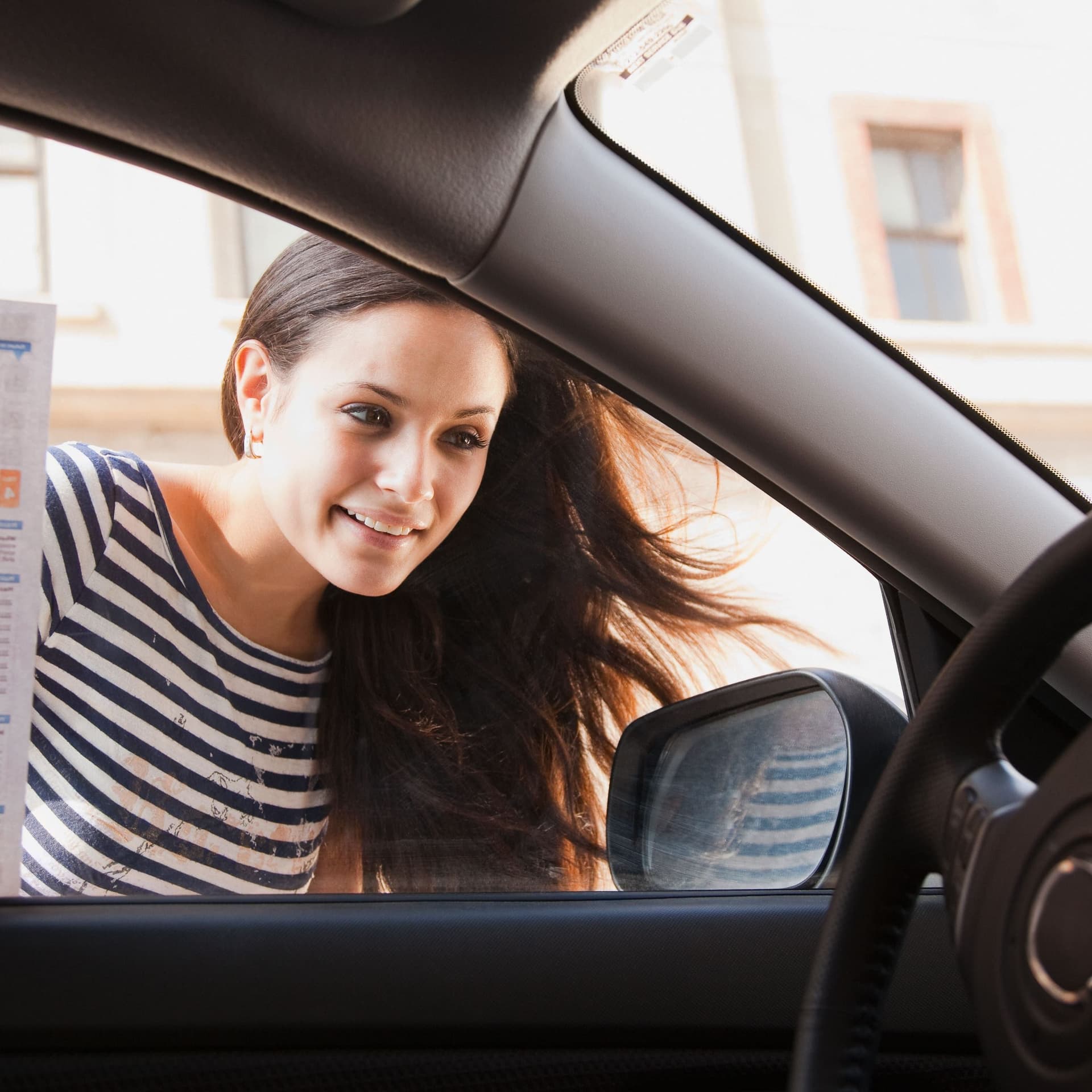 Junge Frau blickt in ein Auto und lächelt.