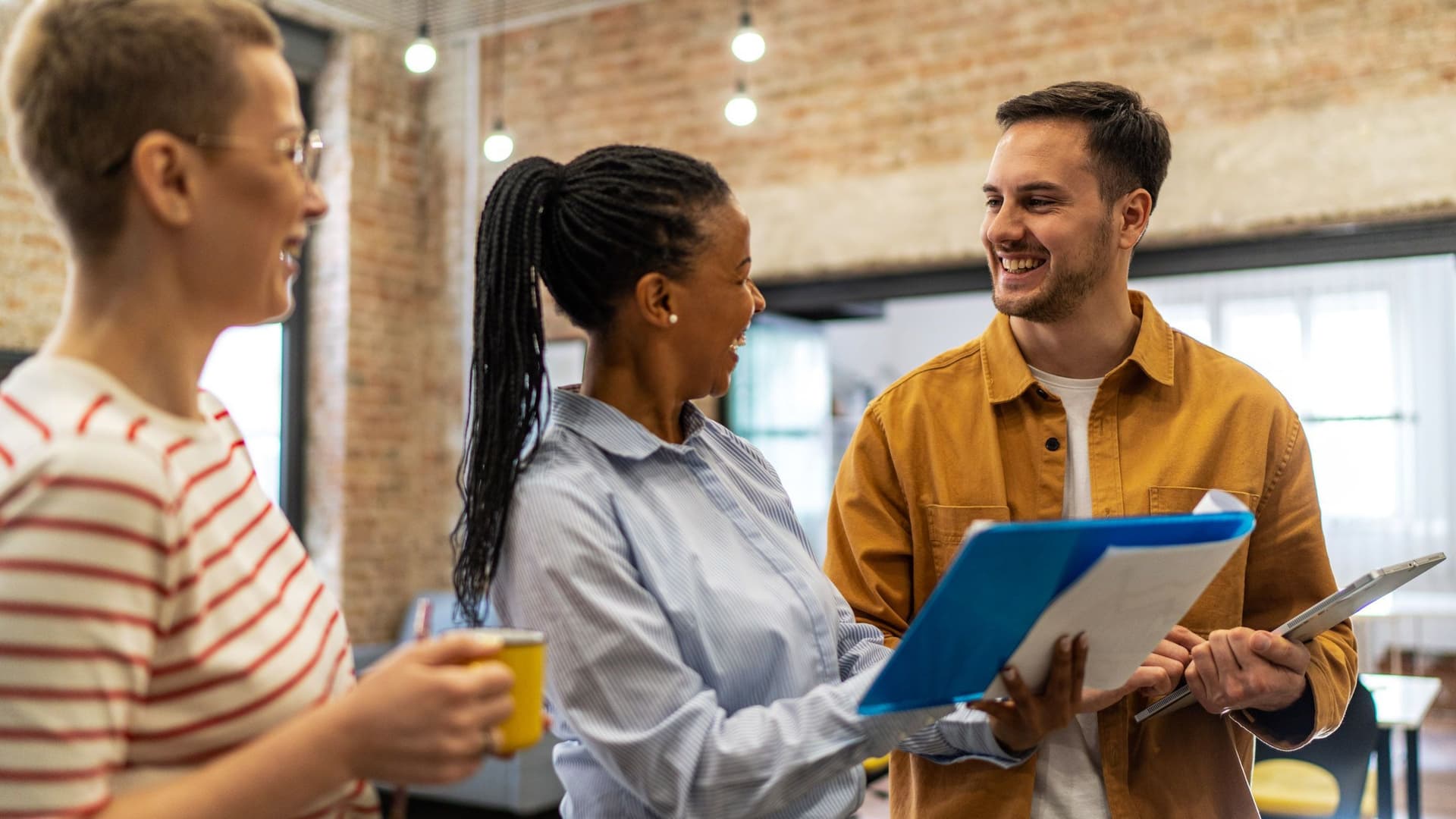 Drei Personen stehen lachend zusammen, einer hält ein Tablet, eine ein Klemmbrett.