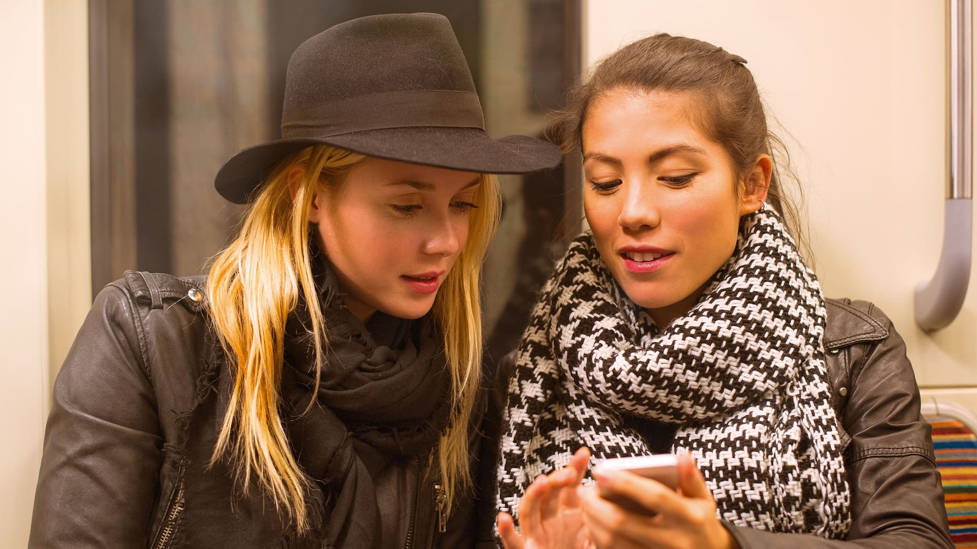 Zwei Frauen sitzen in der Bahn und schauen auf ein Handy.