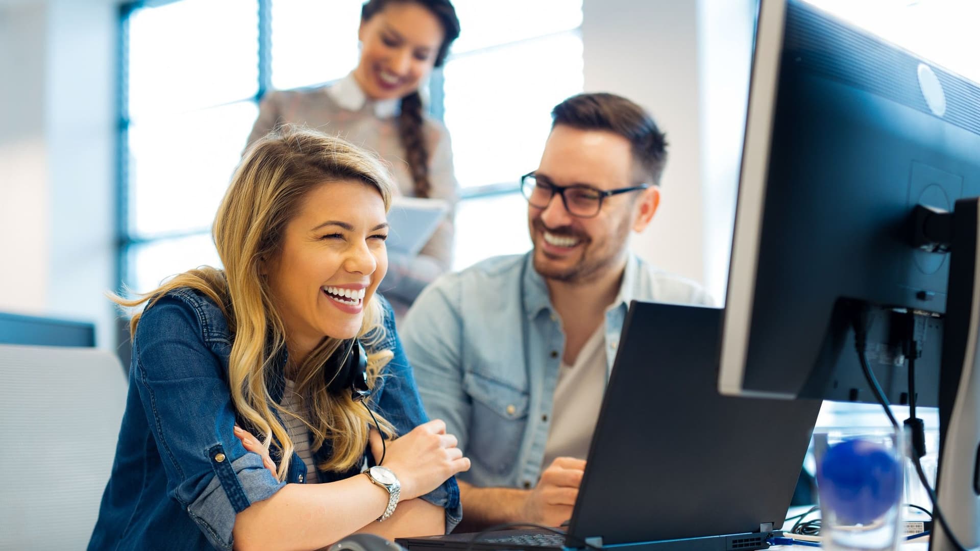 Drei Personen am Computer, alle lachen.
