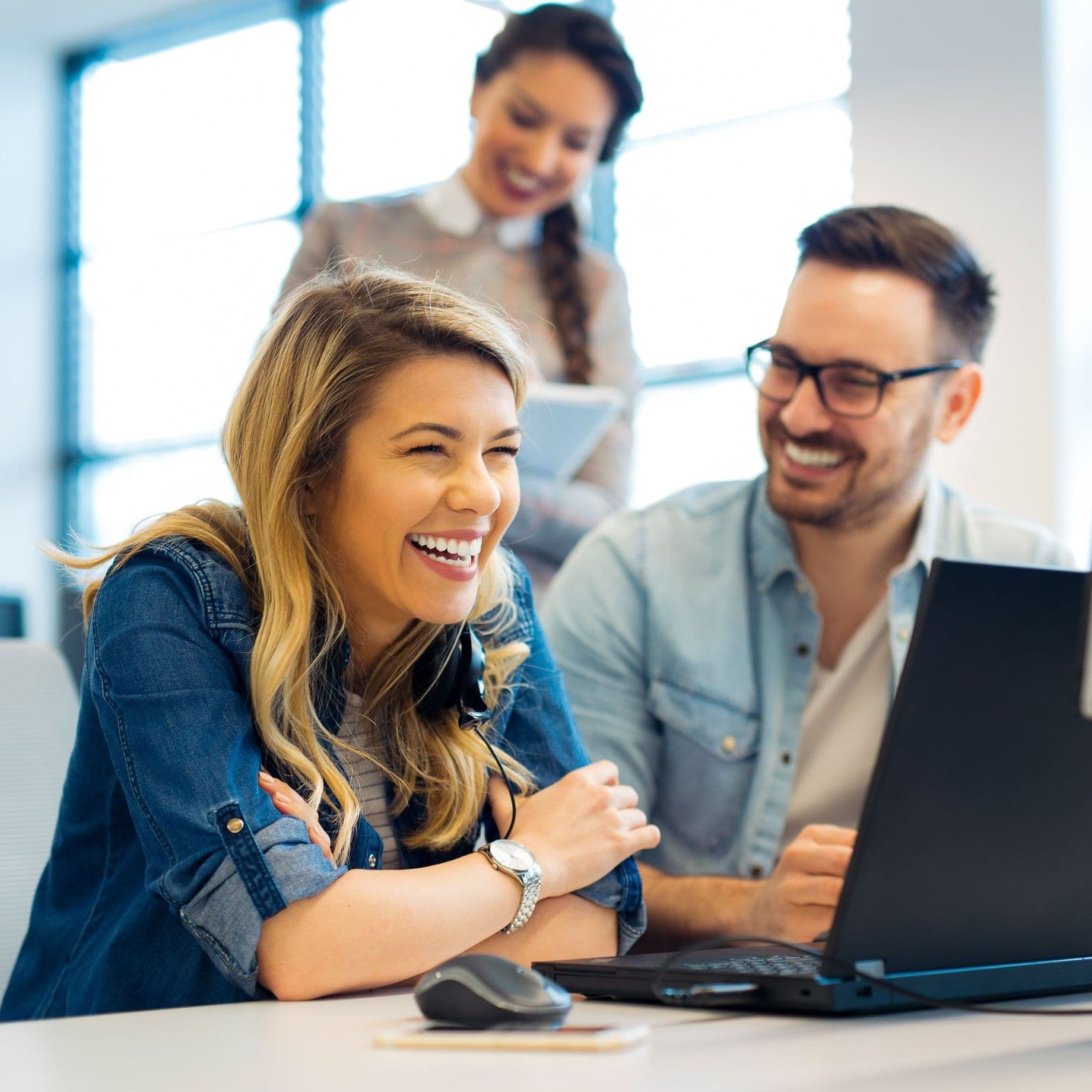 Drei Personen am Computer, alle lachen.